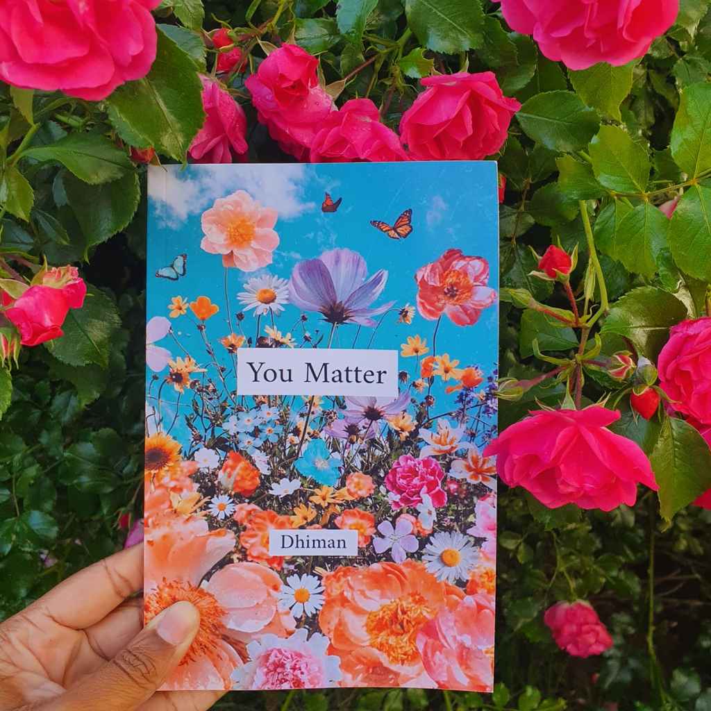 the book 'You Matter' by Dhiman in front of a bright pink rose bush.
